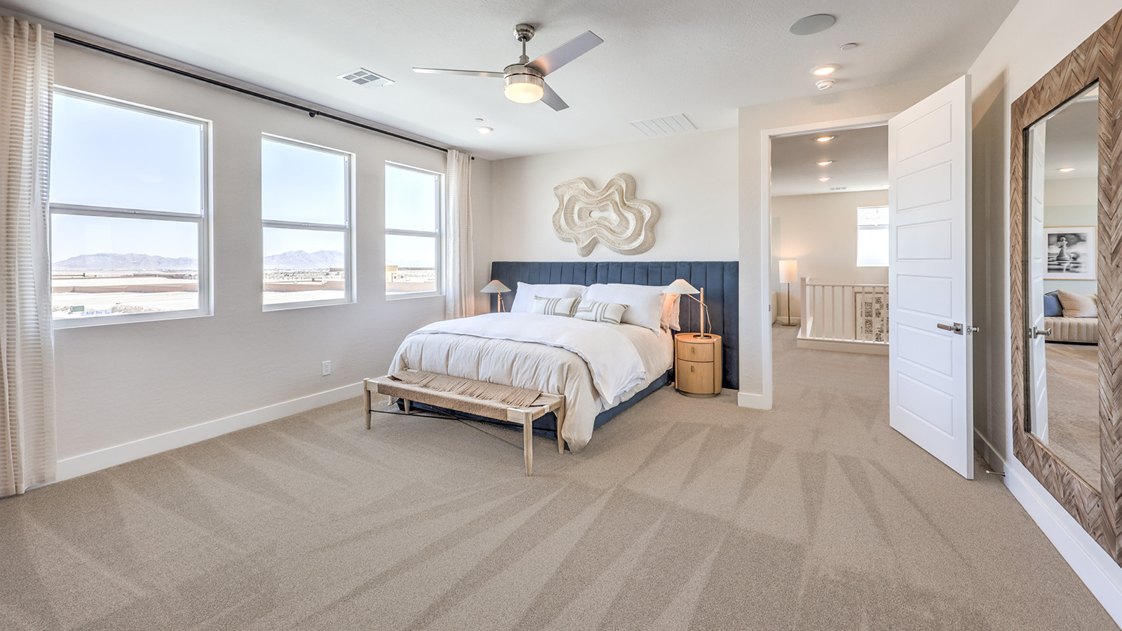 The Bedroom One Suite in our Heartland Summit 3765 model with carpet flooring, large windows, and a ceiling fan with a light kit.