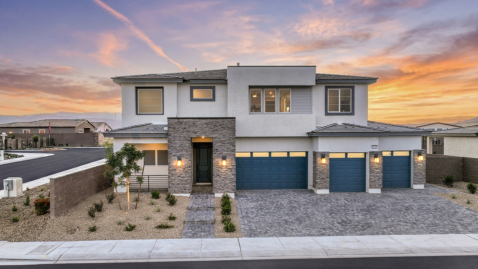 Our 4418 model home in the Heartland Summit community with grey and navy exterior paint schemes, a flat tile roof, front yard landscaping, paver walkways, and a four-car garage.