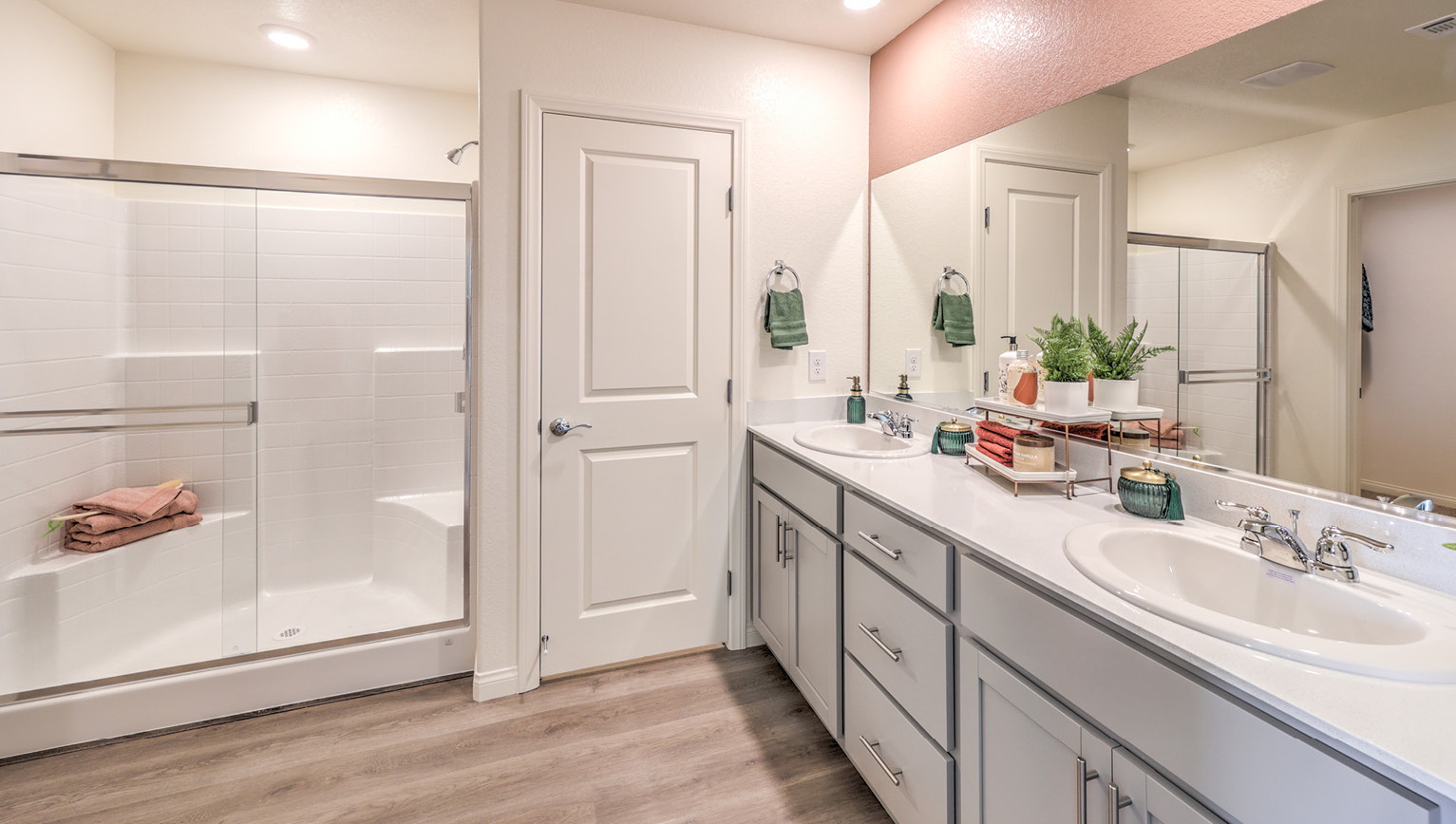 Attached to the Bedroom One Suite, our 1865 model bathroom with granite countertops at the double Bath Vanity, a walk-in shower, mirror, and grey cabinets.