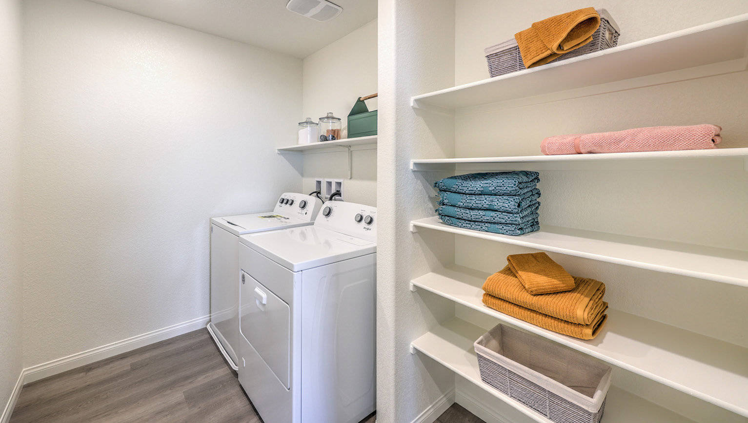 Our Heartland Bay 1865 model laundry room with shelves and a washer and dryer.