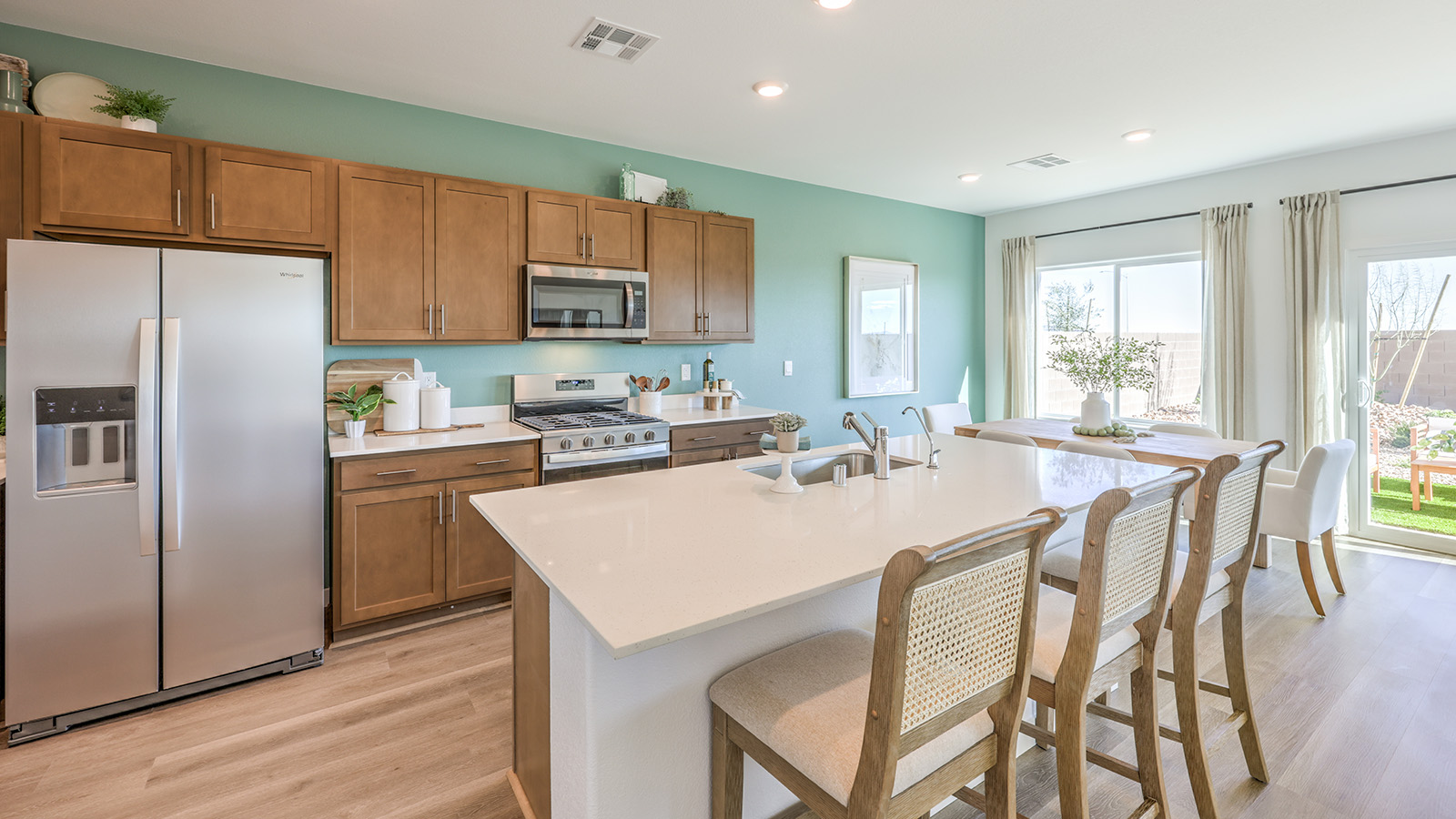 Our 1802 model kitchen in the Heartland Bay Community with brown shaker style cabinets, Quartz countertops, a kitchen island, large pantry, and Whirlpool Stainless Steel appliances.