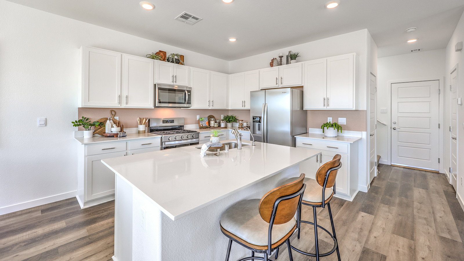 Our 1872 model kitchen in the Heartland Bay Community with white shaker style cabinets, Granite Slab countertops, a kitchen island, and Whirlpool Stainless Steel appliances.