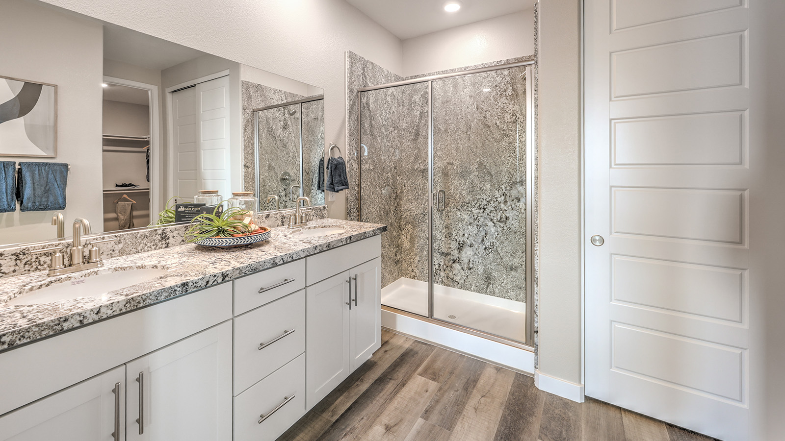Attached to the Bedroom One Suite, our 1839 model bathroom with quartz/marble fusion countertops at the double Bath Vanity, a walk-in shower, walk-in closet, mirror, and grey cabinets.