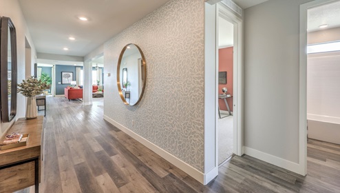 A modern home entrance with 9-foot flat ceilings and luxury vinyl plank flooring. The hallway leads to an open living area with large windows. To the right, are three doorways which provide access to two bedrooms and a bathroom.