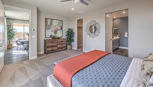 The main bedroom in our Heartland Manor 2754 Plan features plush carpet flooring, a spacious layout, and large windows that bring in natural light. A ceiling fan is centrally located for comfort, and an open doorway leads to the en-suite bathroom. The room also includes a walk-in closet, providing ample storage space.