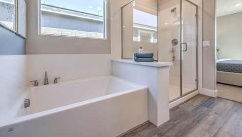 The main bathroom in our Heartland Manor 2754 Plan features a separate tub and shower with quartz or granite surrounds and a glass enclosure. The soaking tub is positioned beneath a window for natural light, while the spacious shower offers a sleek, modern design. Luxury vinyl plank flooring extends throughout, creating a seamless and stylish look.