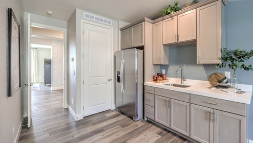 The kitchenette in the MultiGEN suite of our Heartland Manor 2754 Plan features luxury vinyl plank flooring, quartz or granite countertops, and ample cabinet storage. A stainless steel refrigerator and a built-in sink add convenience, creating a functional space for independent living. Designed for multi-generational flexibility, this kitchenette provides both comfort and practicality.