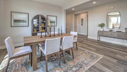 The dining room in our Heartland Manor 2754 Plan features luxury vinyl plank flooring, a spacious layout, and an open-concept design. Natural light streams in from nearby windows, and the room flows seamlessly into the adjacent hallway, enhancing the open feel of the home.