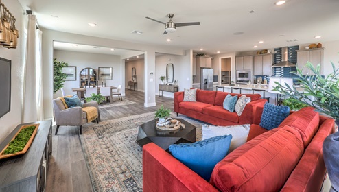 The great room in our Heartland Manor 2754 Plan features luxury vinyl plank flooring, an open-concept layout, and large windows that bring in natural light. The space flows seamlessly into the kitchen, creating a connected and spacious living area. A ceiling fan is centrally located, and sliding glass doors provide easy access to the backyard.