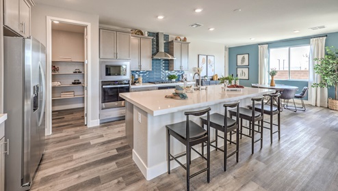 The kitchen in our Heartland Manor 2754 Plan features luxury vinyl plank flooring, an open-concept design, and a spacious layout. A large island with seating provides ample counter space, complemented by quartz or granite countertops with a 2¼-inch edge. Whirlpool stainless steel appliances include a five-burner cooktop, built-in ovens, a microwave, and a dishwasher. The space also features 42-inch upper cabinets for extra storage and a walk-in pantry for added convenience. Large windows bring in natural light, creating a bright and inviting atmosphere.