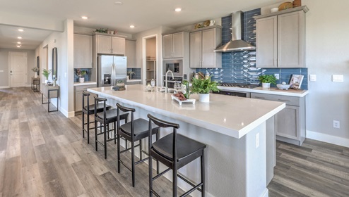 The kitchen in our Heartland Manor 2754 Plan features luxury vinyl plank flooring, an open-concept design, and a spacious layout. A large island with seating provides ample counter space, complemented by quartz or granite countertops with a 2¼-inch edge. Whirlpool stainless steel appliances include a five-burner cooktop, built-in ovens, a microwave, and a dishwasher. The space also features 42-inch upper cabinets for extra storage and a walk-in pantry for added convenience. Large windows bring in natural light, creating a bright and inviting atmosphere.