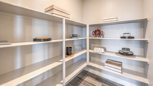 The walk-in pantry in our Heartland Manor 2754 Plan features built-in shelving for ample storage and organization. The open layout provides easy access to kitchen essentials, while luxury vinyl plank flooring extends from the kitchen for a seamless look. This spacious pantry adds both convenience and functionality to the home.