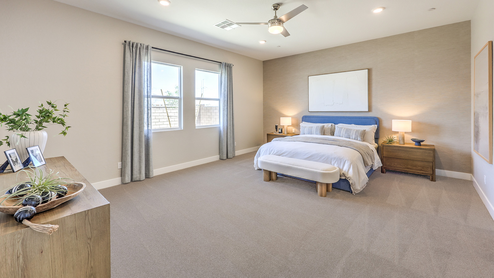 The main bedroom in our Heartland Manor 2538 Plan features plush carpet flooring, a spacious layout, and large windows that bring in natural light. A ceiling fan is centrally located for comfort, and an open doorway leads to the en-suite bathroom. The room also includes a walk-in closet, providing ample storage space.