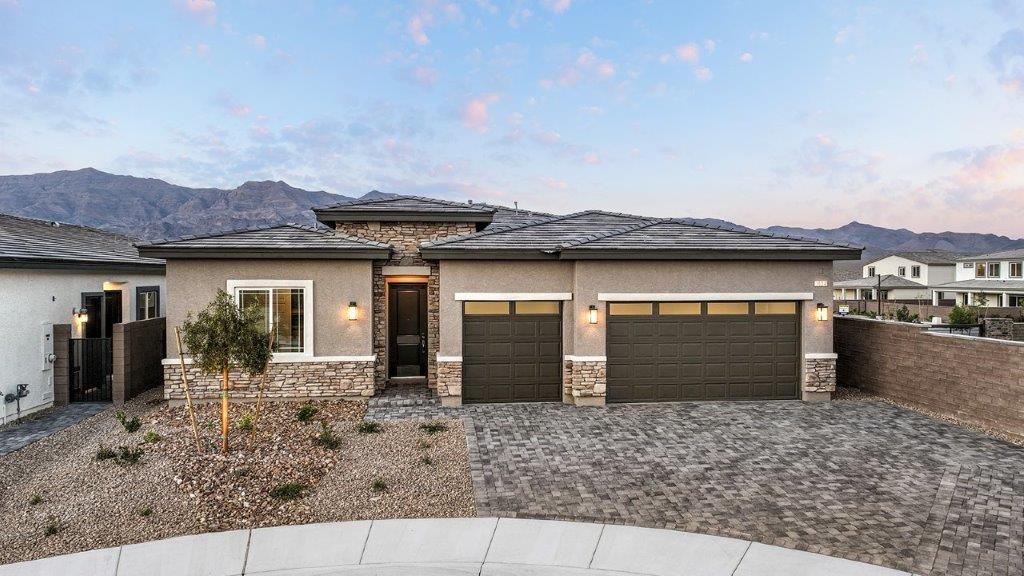 Our 2538 model home in the Heartland Manor community with tan exterior paint schemes, a flat tile roof, front yard landscaping, paver walkways, and a three-car garage.