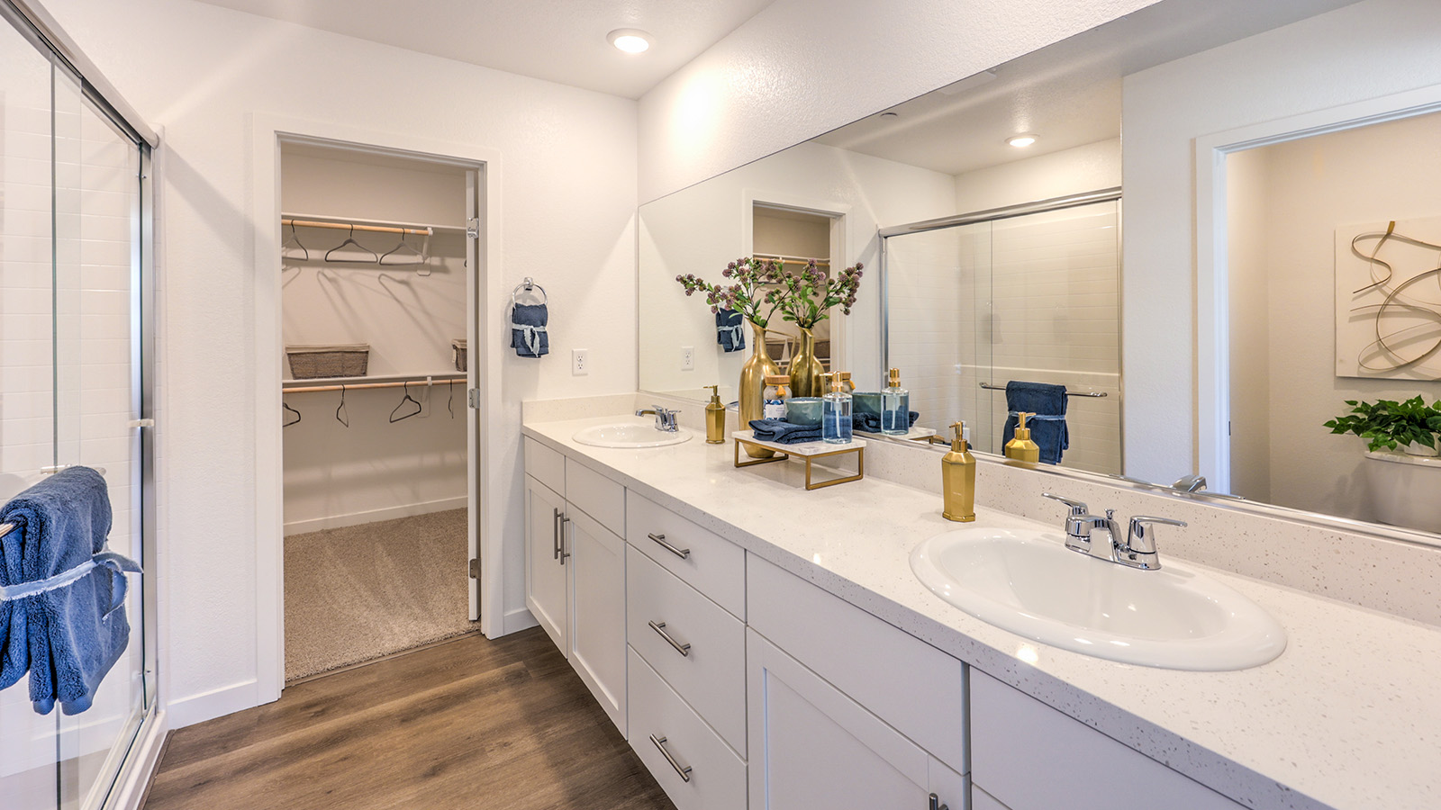 Attached to the Bedroom One Suite, our 1865 model bathroom with granite countertops at the double Bath Vanity, a walk-in shower, mirror, and white cabinets.