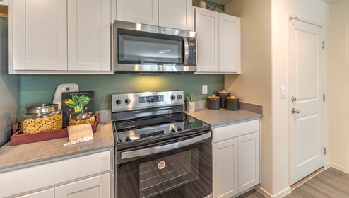 Our 1309 model kitchen in the Canyon Trails Community with white shaker style cabinets, quartz countertops, a kitchen island, and Whirlpool Stainless Steel appliances.