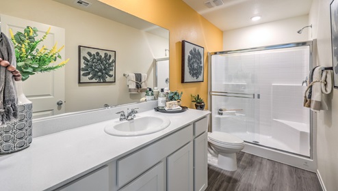 Attached to the Bedroom One Suite, our 1309 model bathroom with quartz/marble fusion countertops at the Bath Vanity, a walk-in shower, mirror, and white cabinets.