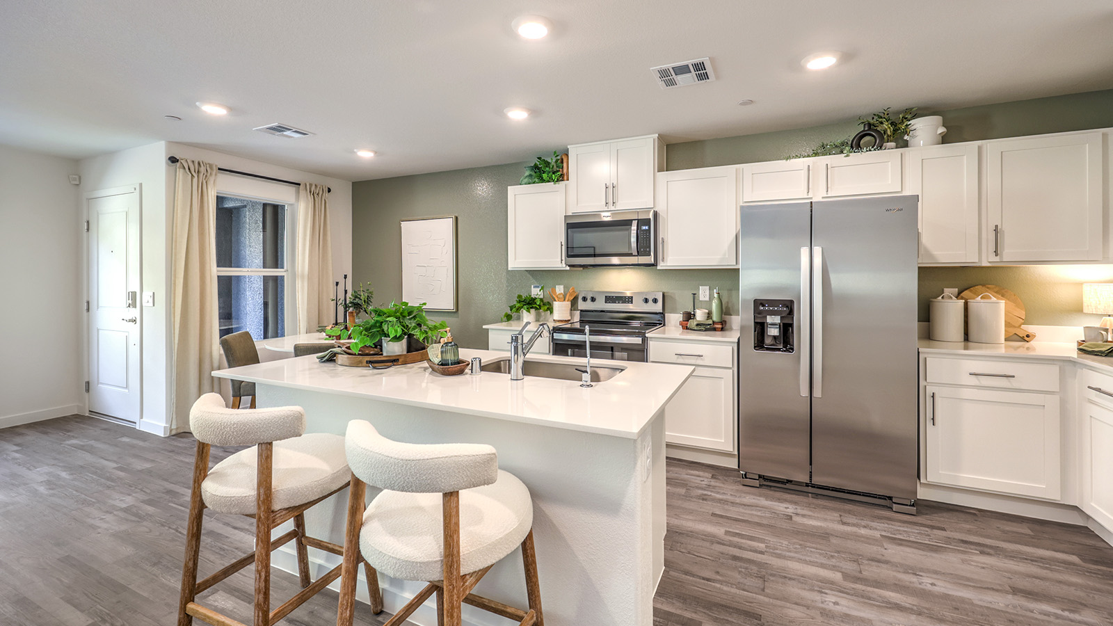Our 1410 model kitchen in the Canyon Trails Community with white shaker style cabinets, quartz countertops, a kitchen island/seating area, and Whirlpool Stainless Steel appliances.