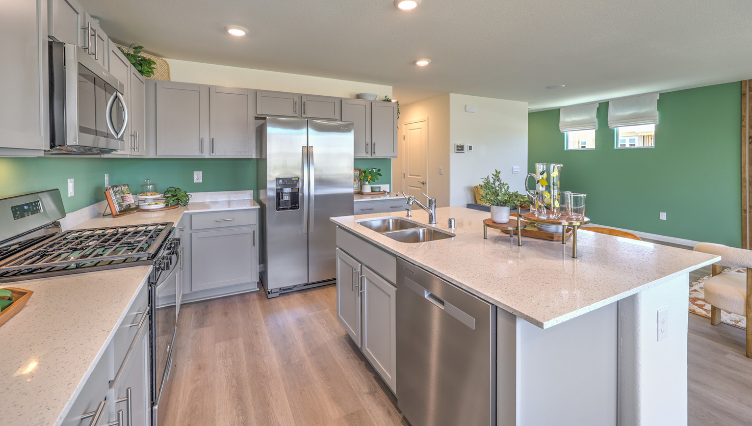 Our 1865 model kitchen in the Kalea Bay Community with grey shaker style cabinets, quartz countertops, a kitchen island, and Whirlpool Stainless Steel appliances.