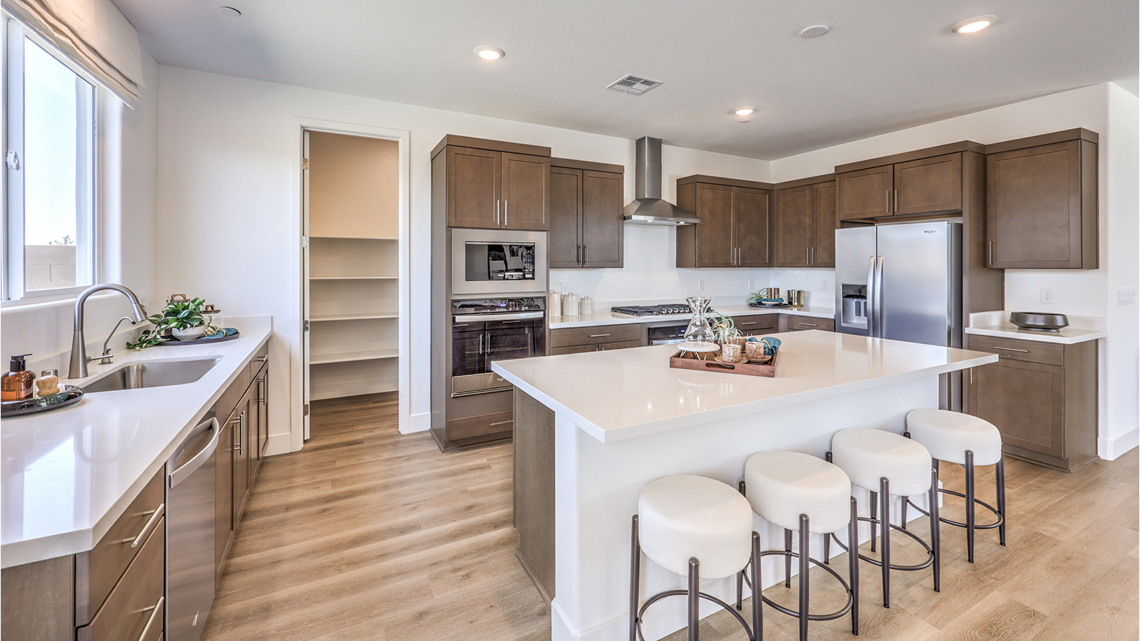Our 3000 model kitchen in the Heartland Falls Community with brown shaker style cabinets, Granite Slab countertops, a kitchen island, window, and Whirlpool Stainless Steel appliances.