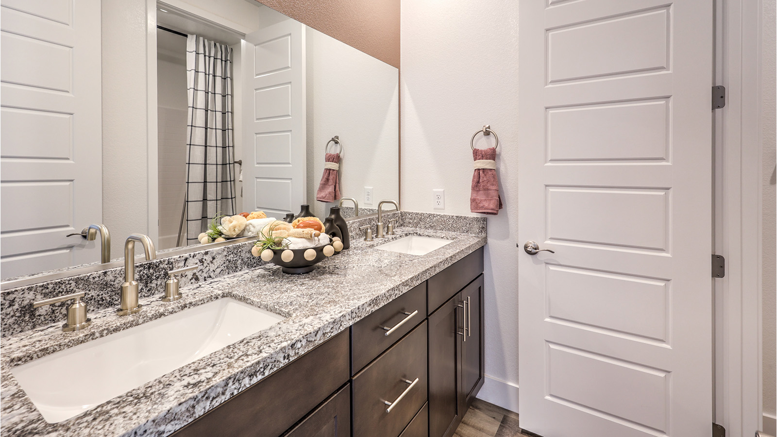 Bathroom Three in our Heartland Falls 2600 model with Granite countertops at the double Bath Vanity, a shower, mirror, and white cabinets.