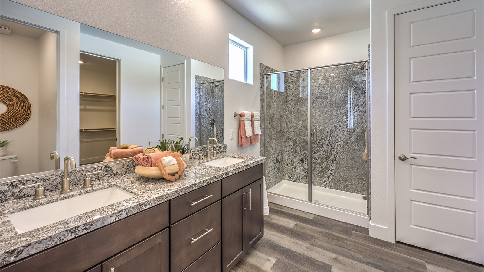Attached to the Bedroom One Suite, our 2660 model bathroom with granite countertops at the double Bath Vanity, a walk-in shower, walk-in closet, mirror, and grey cabinets.