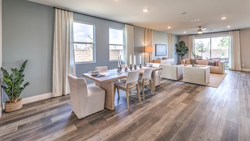 The dining room and great room in our Heartlnad Falls 3-Car Plan features an open-concept design with 9-foot flat ceilings and luxury vinyl plank flooring. The dining area is spacious, with a large window allowing natural light to fill the space. Adjacent to it, the great room offers a bright and airy feel, enhanced by additional windows and sliding glass doors leading to the backyard. The seamless flow between these areas creates a welcoming and functional living space.