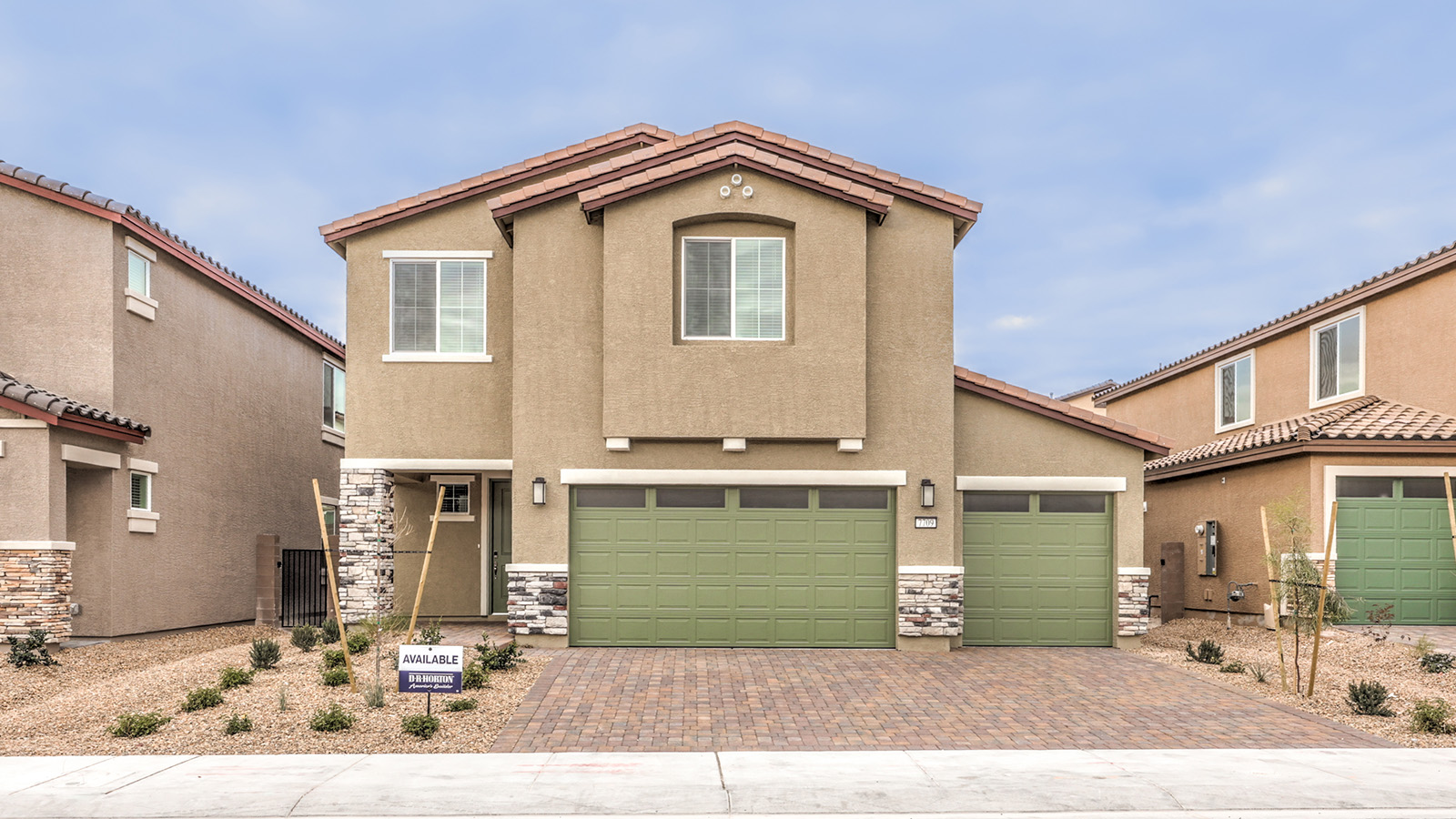 Our 2436 model home in the Heartland Falls community with tan and green exterior paint schemes, a flat tile roof, 3-car garage, front yard landscaping, and paver walkways.
