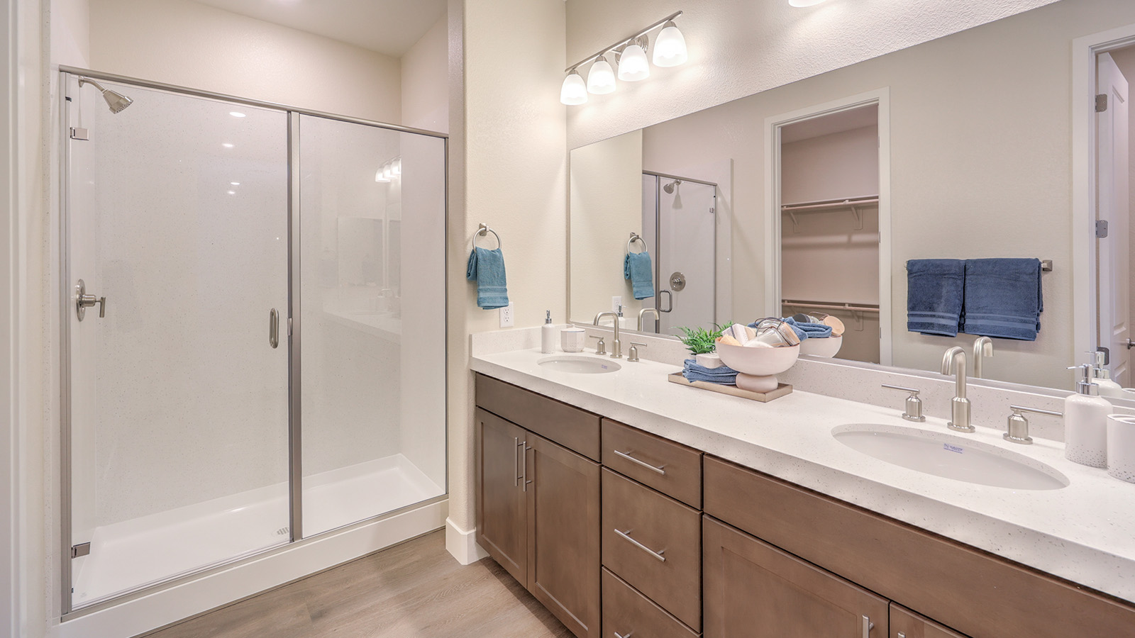 Attached to the Bedroom One Suite, our 2436 model bathroom with quartz/marble fusion countertops at the double Bath Vanity, a walk-in shower, walk-in closet, mirror, and grey cabinets.