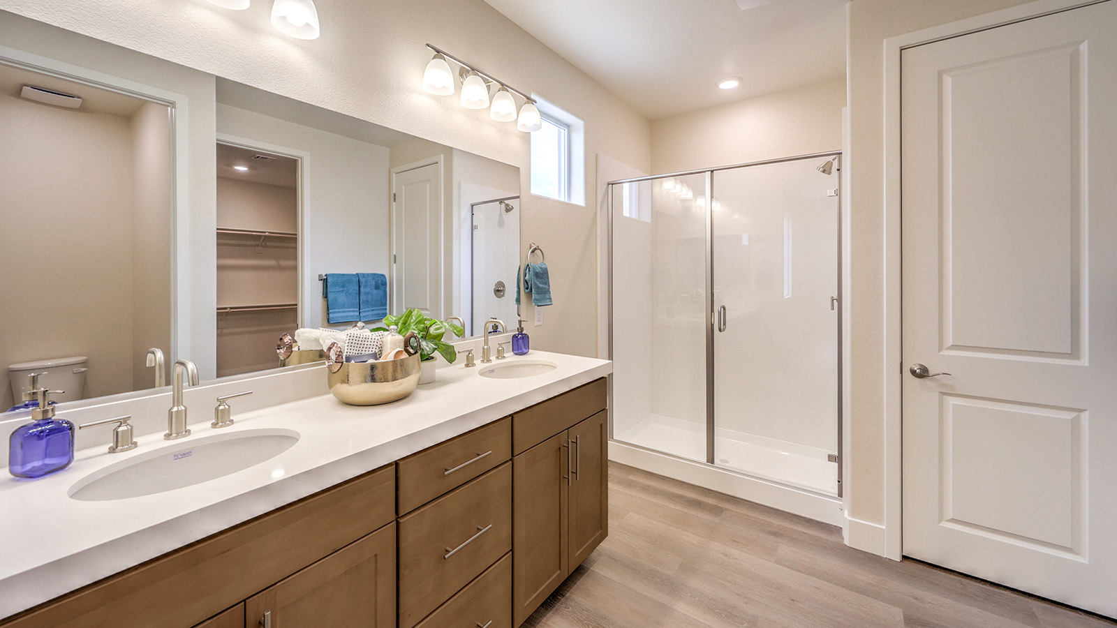 Attached to the Bedroom One Suite, our 2660 model bathroom with granite countertops at the double Bath Vanity, a walk-in shower, walk-in closet, mirror, and brown cabinets.