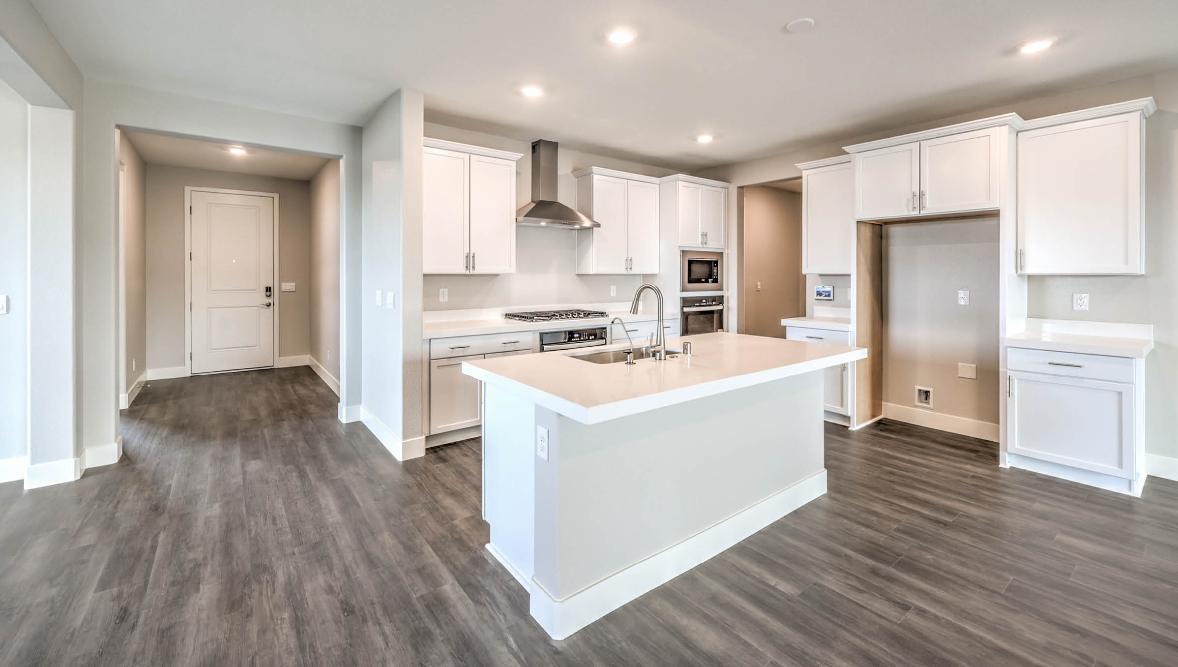The Heartland Manor 2300 Plan Kitchen featuring Luxury Vinyl Plank flooring, granite countertops with a large center island, and a herringbone tile backsplash. Equipped with Whirlpool Stainless Steel Appliances including a 5-burner cooktop, built-in microwave, and dishwasher, this kitchen is designed for both functionality and modern style.