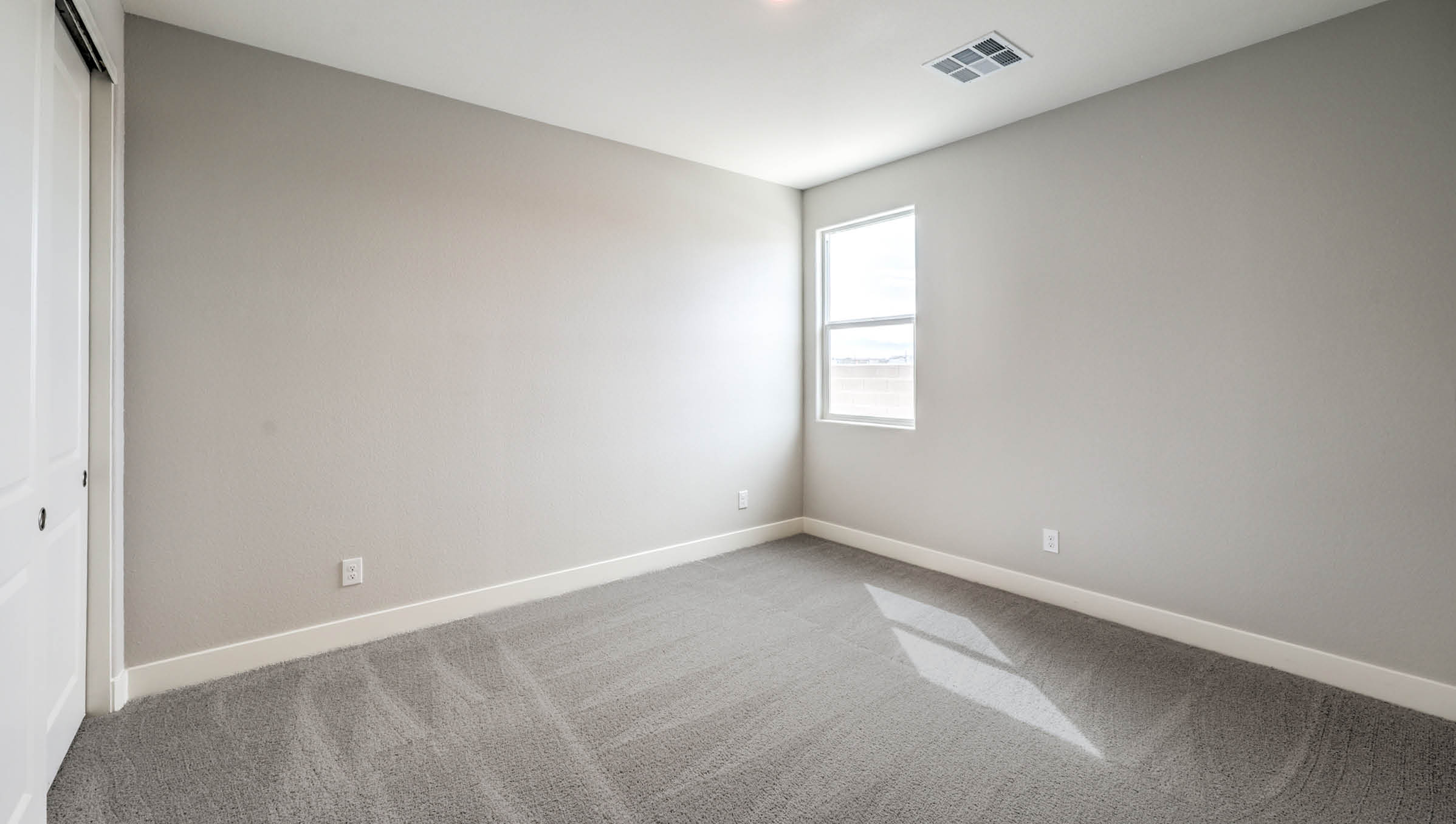 The Heartland Manor 2300 Plan Bedroom 2 featuring plush wall-to-wall carpet, a large window for natural light, and a double-door closet for storage. Conveniently located near shared living spaces, this versatile bedroom is ideal for guests, family members, or a home office.