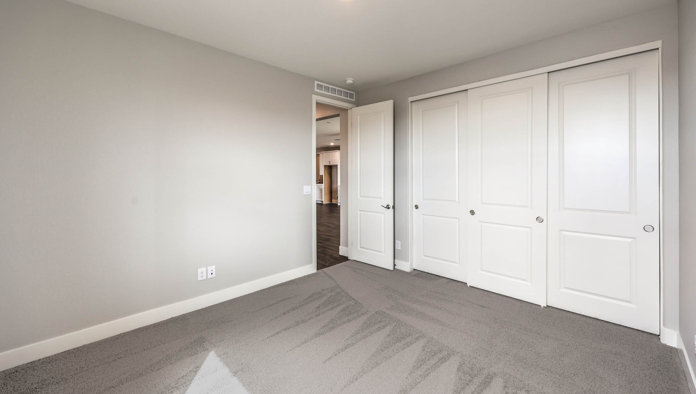 The Heartland Manor 2300 Plan Bedroom 2 featuring plush wall-to-wall carpet, a large window for natural light, and a double-door closet for storage. Conveniently located near shared living spaces, this versatile bedroom is ideal for guests, family members, or a home office.