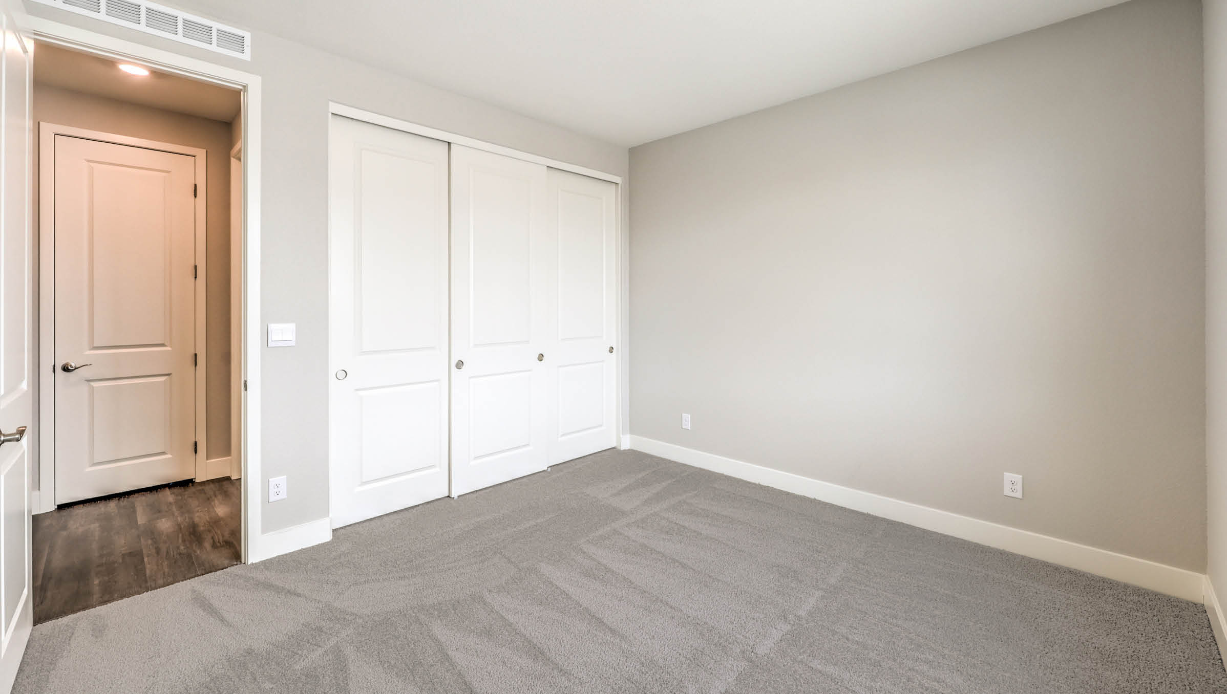 The Heartland Manor 2300 Plan Bedroom 4 featuring plush wall-to-wall carpet, a spacious layout, and a double-door closet for ample storage. Conveniently located near a shared bathroom, this room offers comfort and flexibility for guests, children, or a home office setup.