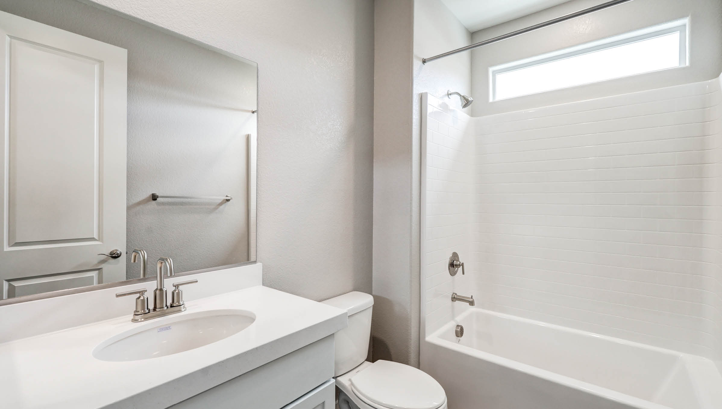 The Heartland Manor 2300 Plan Bathroom 2 featuring Luxury Vinyl Plank flooring, a granite countertop vanity with an undermount sink, and a combination tub and shower with white tile surround. A transom window above the shower provides natural light while maintaining privacy, making this bathroom a bright and functional space for daily use.