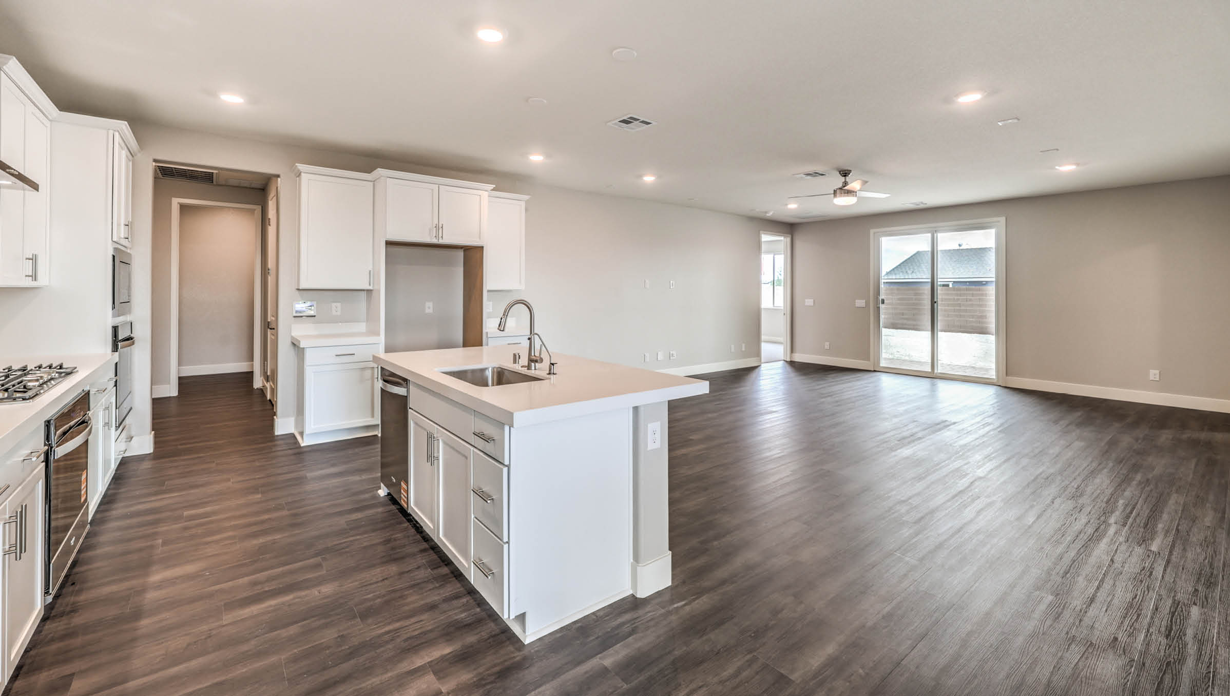 The Heartland Manor 2300 Plan Kitchen featuring Luxury Vinyl Plank flooring, granite countertops with a large center island, and a herringbone tile backsplash. Equipped with Whirlpool Stainless Steel Appliances including a 5-burner cooktop, built-in microwave, and dishwasher, this kitchen is designed for both functionality and modern style.