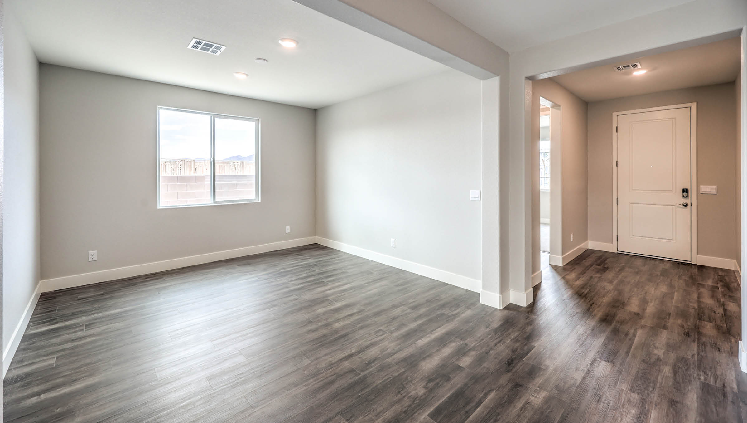 The Heartland Manor 2300 Plan Dining Room featuring Luxury Vinyl Plank flooring, a large front-facing window that brings in natural light, and an open layout connected to the main entry, offering a versatile space for dining or entertaining.