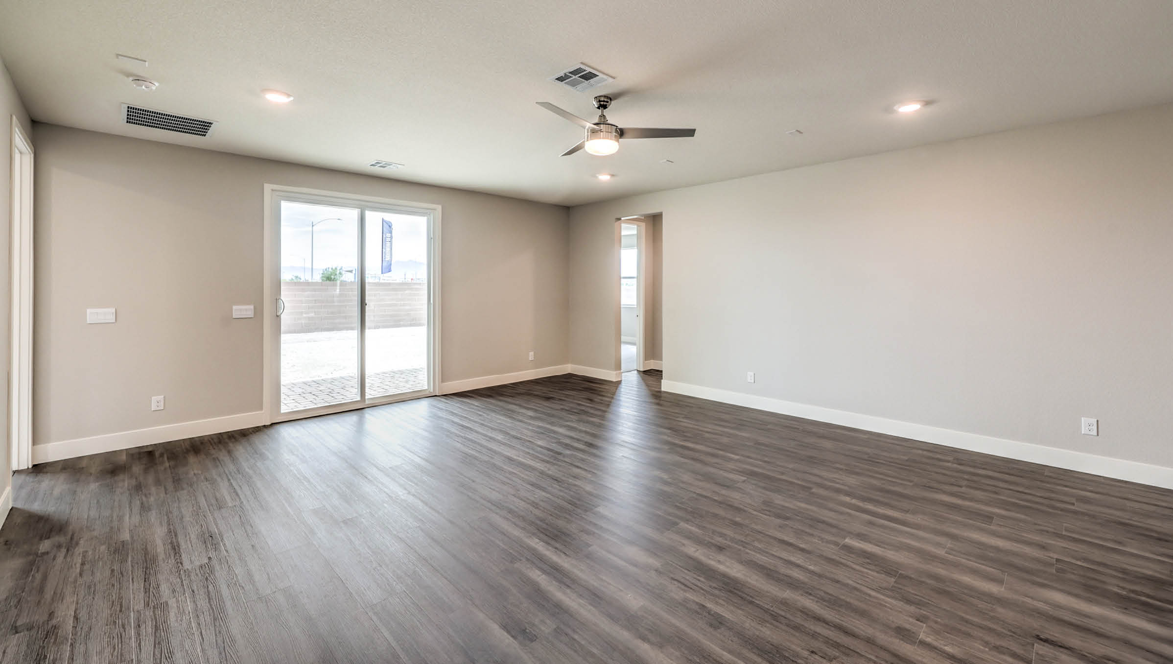 The Heartland Manor 2300 Plan Great Room featuring Luxury Vinyl Plank flooring, a modern ceiling fan, and a large sliding glass door that opens to the backyard. This spacious and open layout offers abundant natural light and seamless flow to adjoining areas, ideal for everyday living and entertaining.