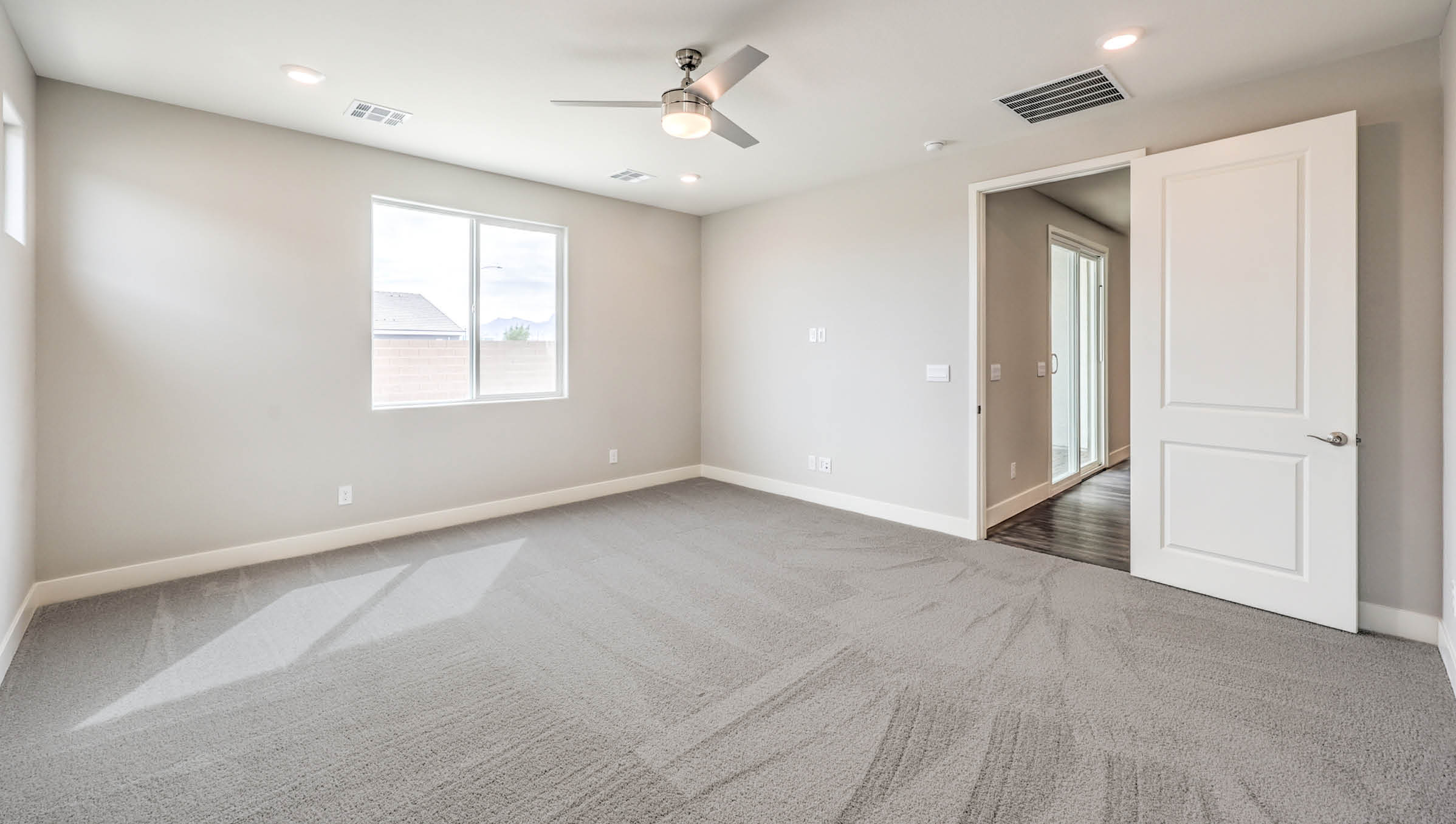 The Heartland Manor 2300 Plan Main Bedroom Suite featuring plush wall-to-wall carpet, multiple windows providing natural light, and a modern ceiling fan. This spacious layout offers a private retreat with direct access to the ensuite bathroom and walk-in closet, designed for comfort and relaxation.