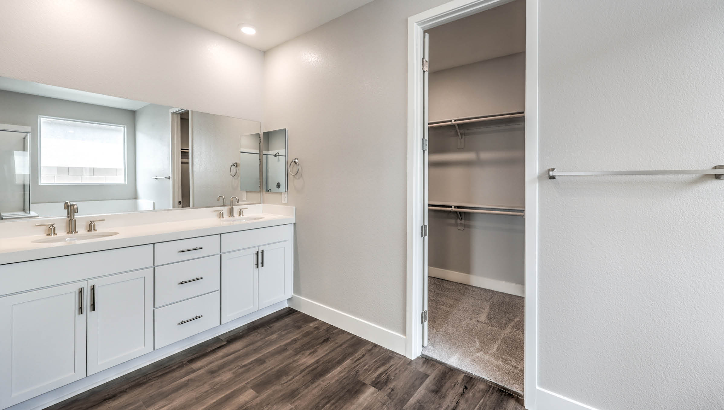 The Heartland Manor 2300 Plan Main Bedroom Suite Bathroom featuring Luxury Vinyl Plank flooring, granite countertops at the dual-sink vanity, and direct access to large walk-in closets. This spacious bathroom offers modern functionality with ample storage and natural light, creating a private and relaxing retreat.