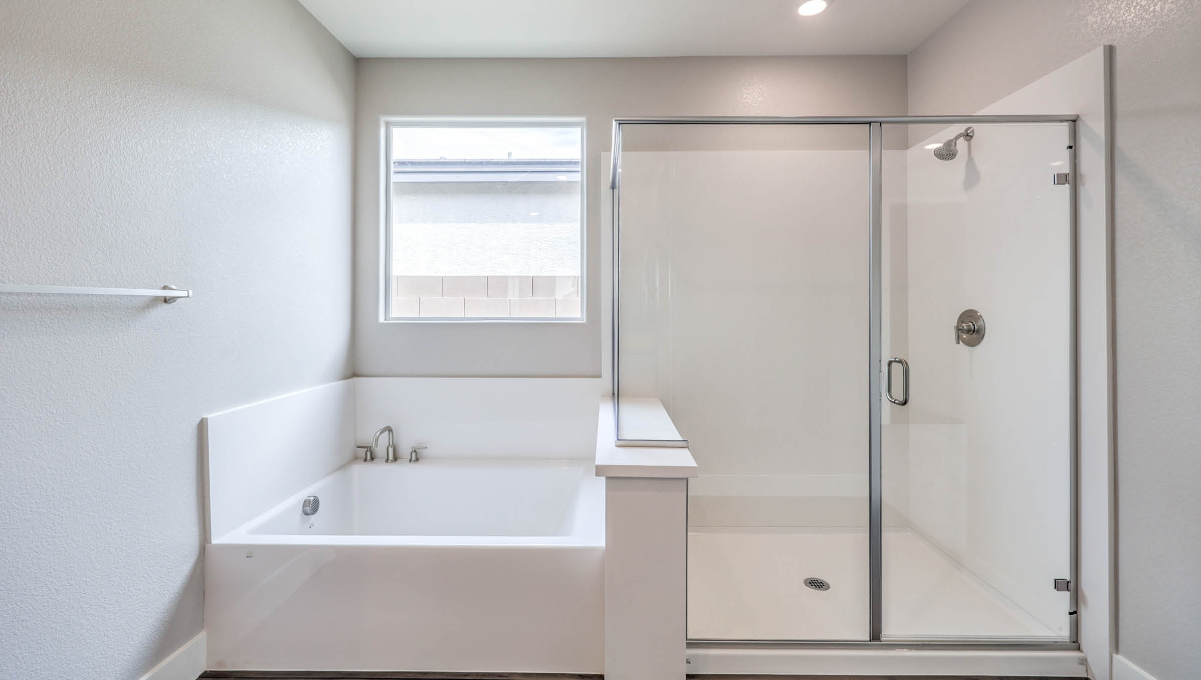 The Heartland Manor 2300 Plan Main Bedroom Suite Bathroom featuring Luxury Vinyl Plank flooring, a separate soaking tub with granite surround, and a walk-in shower with a clear glass enclosure. This spacious layout offers a spa-like retreat with private access to large walk-in closets, blending comfort and elegance.