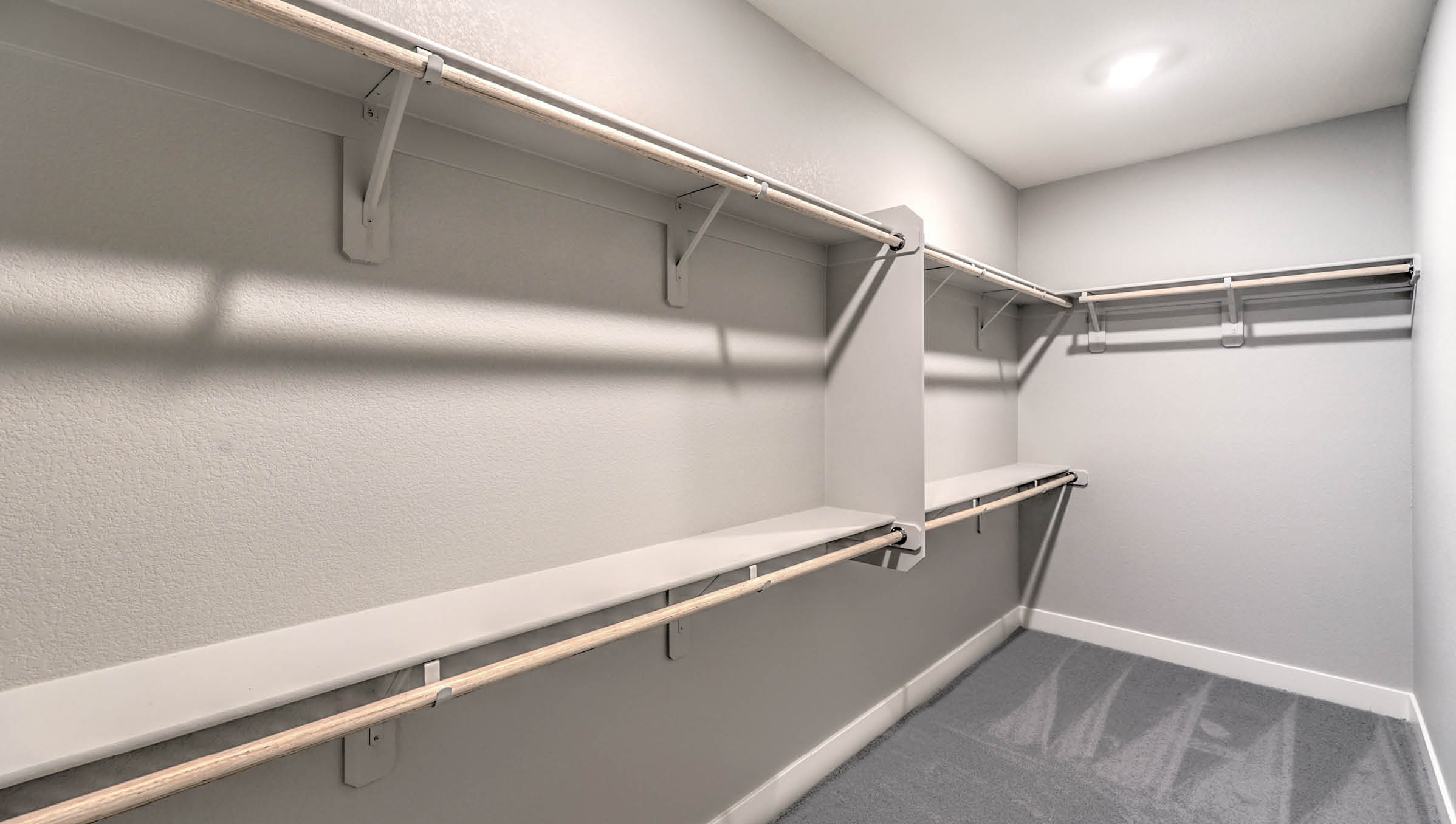 The Heartland Manor 2300 Plan Main Bedroom Suite Walk-In Closet featuring plush wall-to-wall carpet, built-in shelving, and double-level hanging rods. This spacious and well-lit closet offers ample storage and organization, conveniently accessible from the ensuite bathroom for everyday ease and comfort.