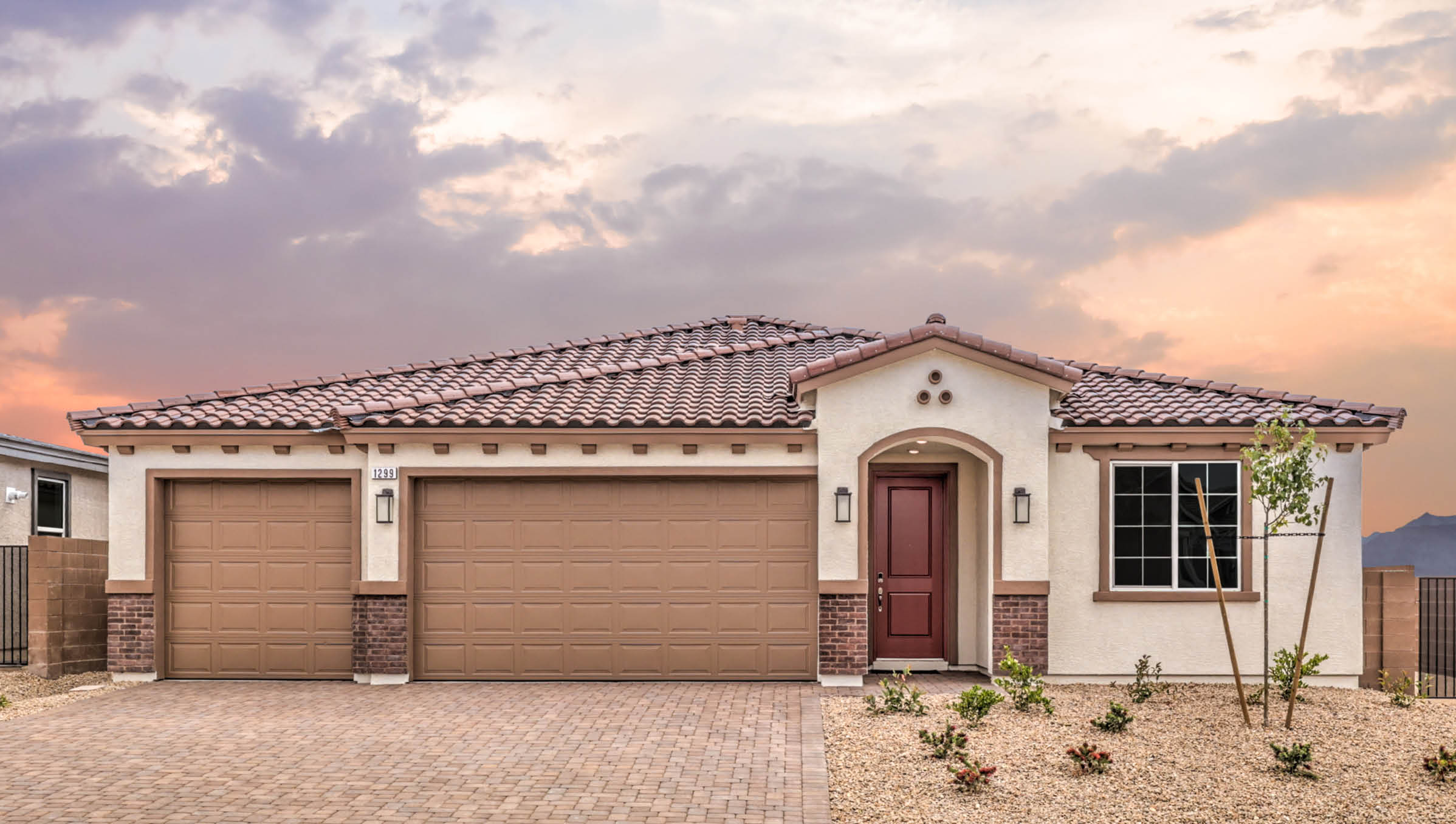 Our 2300 model home in the Heartland Manor community with white and brown exterior paint schemes, a flat tile roof, front yard landscaping, paver walkways, and a three-car garage.