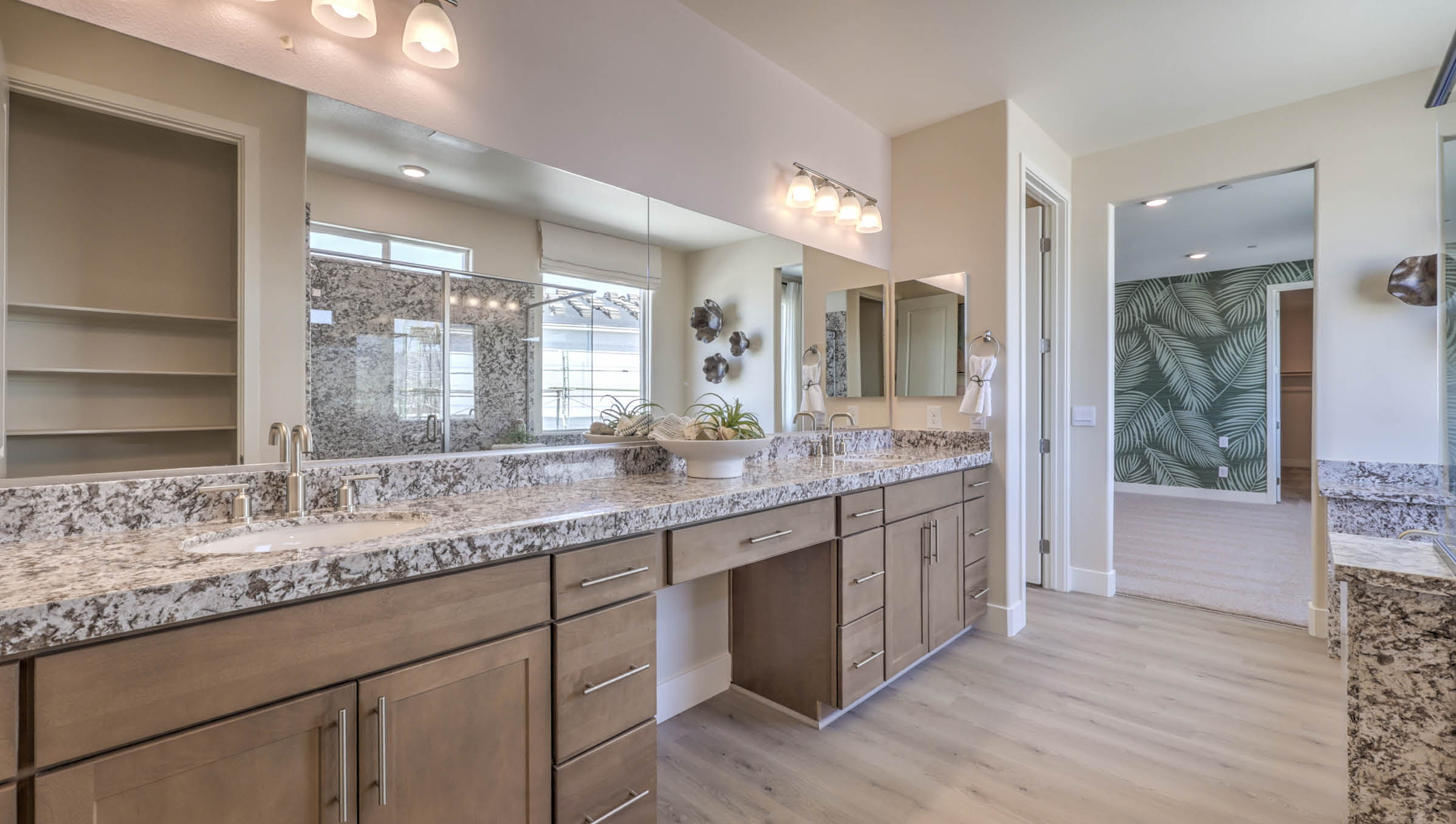 Attached to the Bedroom One Suite, our 4425 model bathroom with granite countertops at the double Bath Vanity, a walk-in closet, mirror, and brown cabinets.