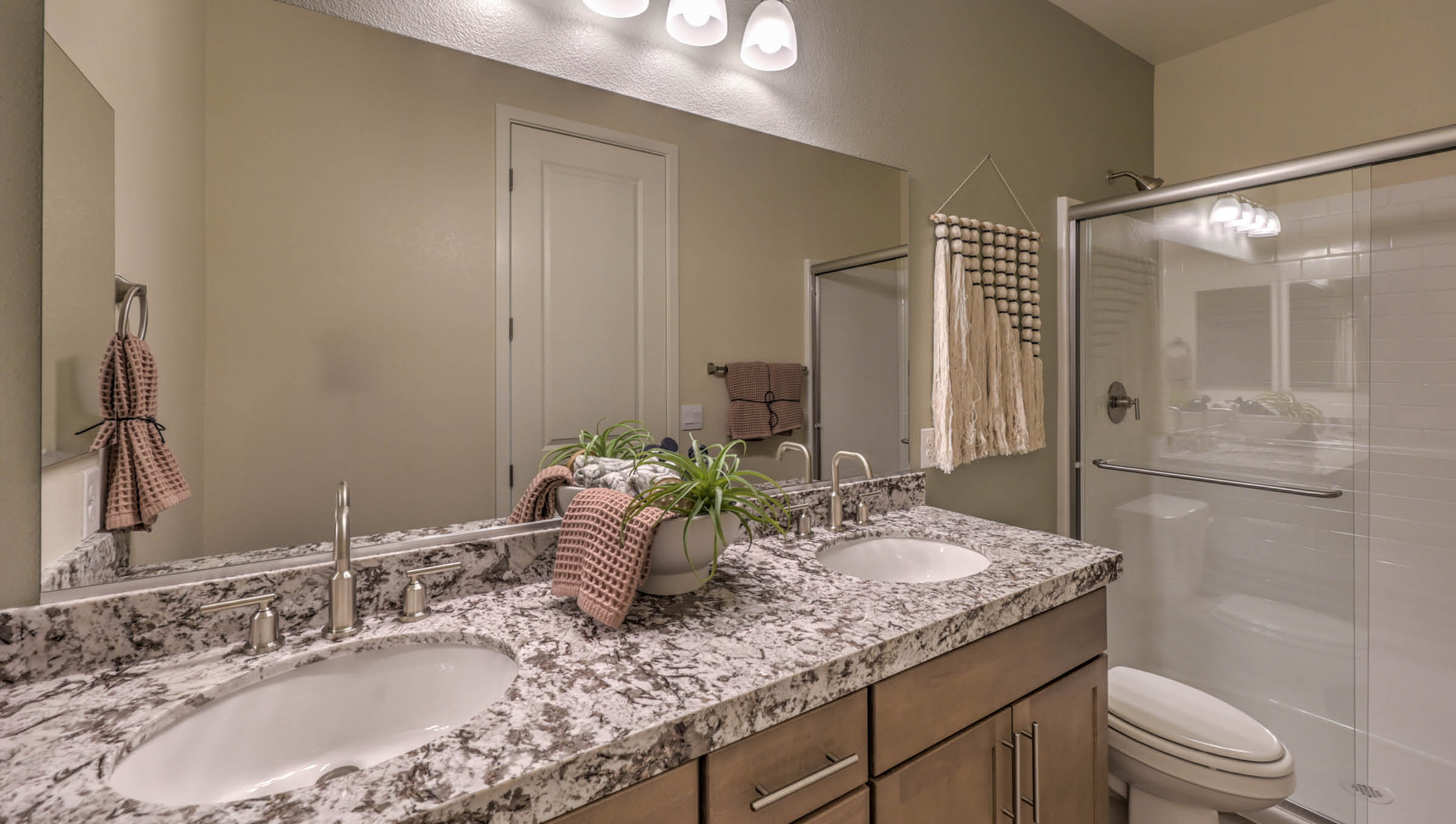 Bathroom Four in our Heartland Summit 4425 Multigen Suite with granite countertops at the Bath Vanity, a walk-in shower, mirror, and brown cabinets.