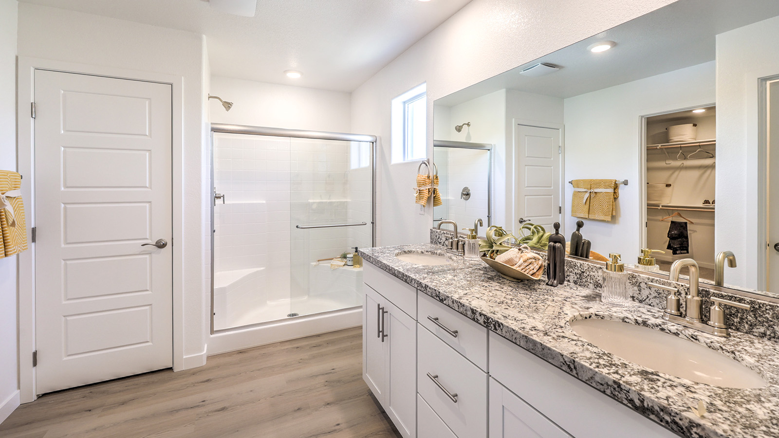 Attached to the Bedroom One Suite, our 2660 model bathroom with quartz countertops at the double Bath Vanity, a walk-in shower, walk-in closet, mirror, and white cabinets.