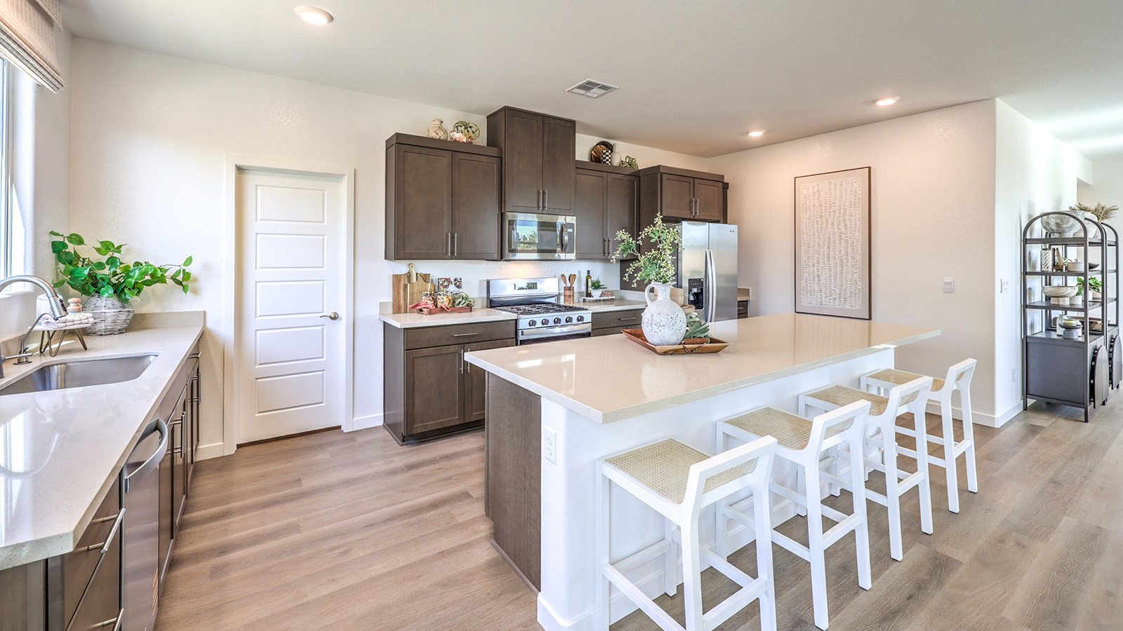 The Tropical Falls 3000 Model Kitchen with Luxury Vinyl Plank flooring, featuring Whirlpool stainless steel appliances, a quartz countertop, and a large center island with seating. The kitchen includes ample cabinetry, a walk-in pantry, and expansive windows that bring in natural light for a bright and functional cooking space.