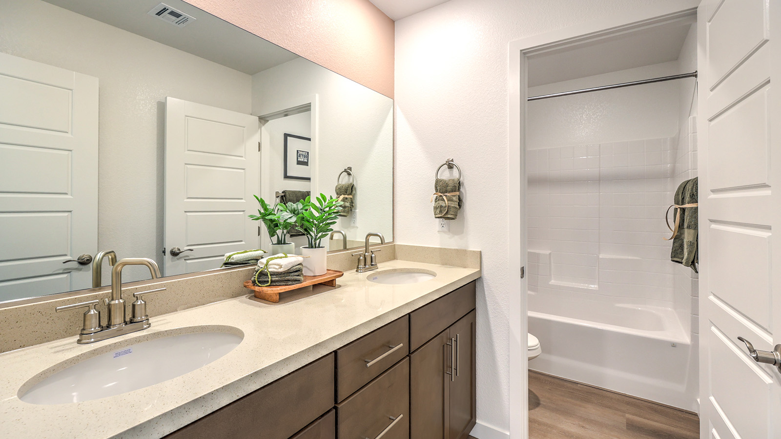 The Tropical Falls 3000 Model Second Bathroom featuring Luxury Vinyl Plank flooring, a quartz countertop with an undermount sink, and a combination tub and shower with white tile surround. The bathroom includes built-in storage, modern fixtures, and is conveniently located near the secondary bedrooms for easy access.