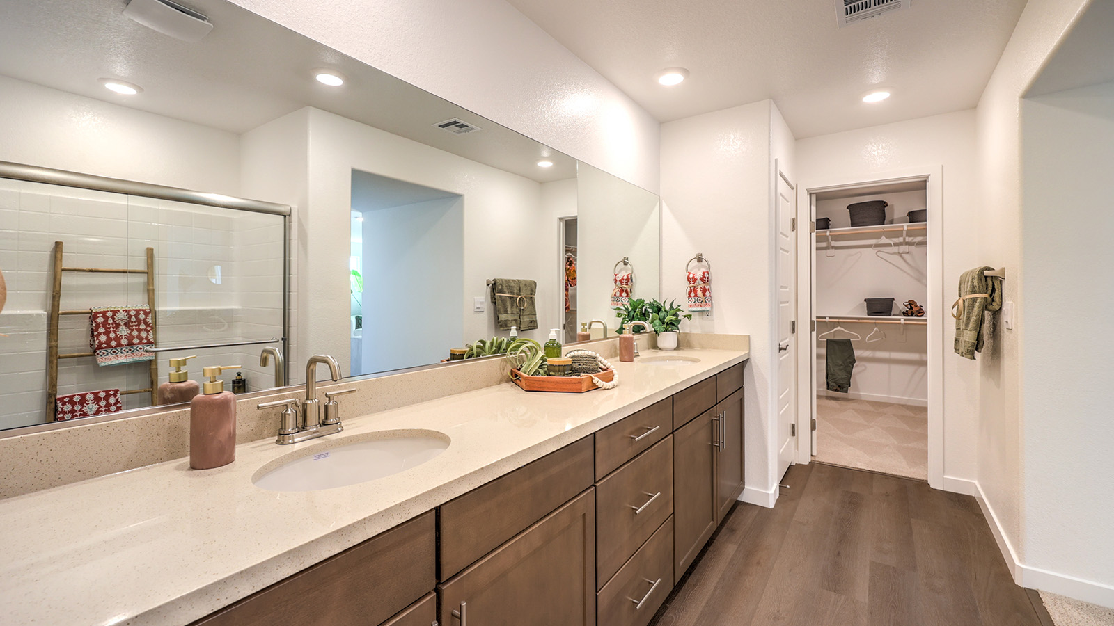 The Tropical Falls 3000 Model Main Bedroom Suite Bathroom featuring Luxury Vinyl Plank flooring, dual sinks with quartz countertops, and a large frameless glass shower. The bathroom offers direct access to a spacious walk-in closet and includes recessed lighting and a full-length mirror for a bright and functional layout.