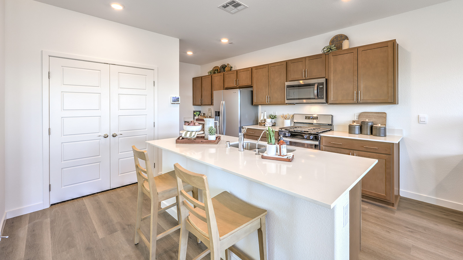 Our 1802 model kitchen in the Meranto Bay Community with brown shaker style cabinets, Quartz countertops, a kitchen island, large pantry, and Whirlpool Stainless Steel appliances.